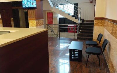 Welcoming hotel lobby featuring a polished reception counter, black guest chairs, coffee table, staircase with stainless steel railings, and glossy tiled flooring.