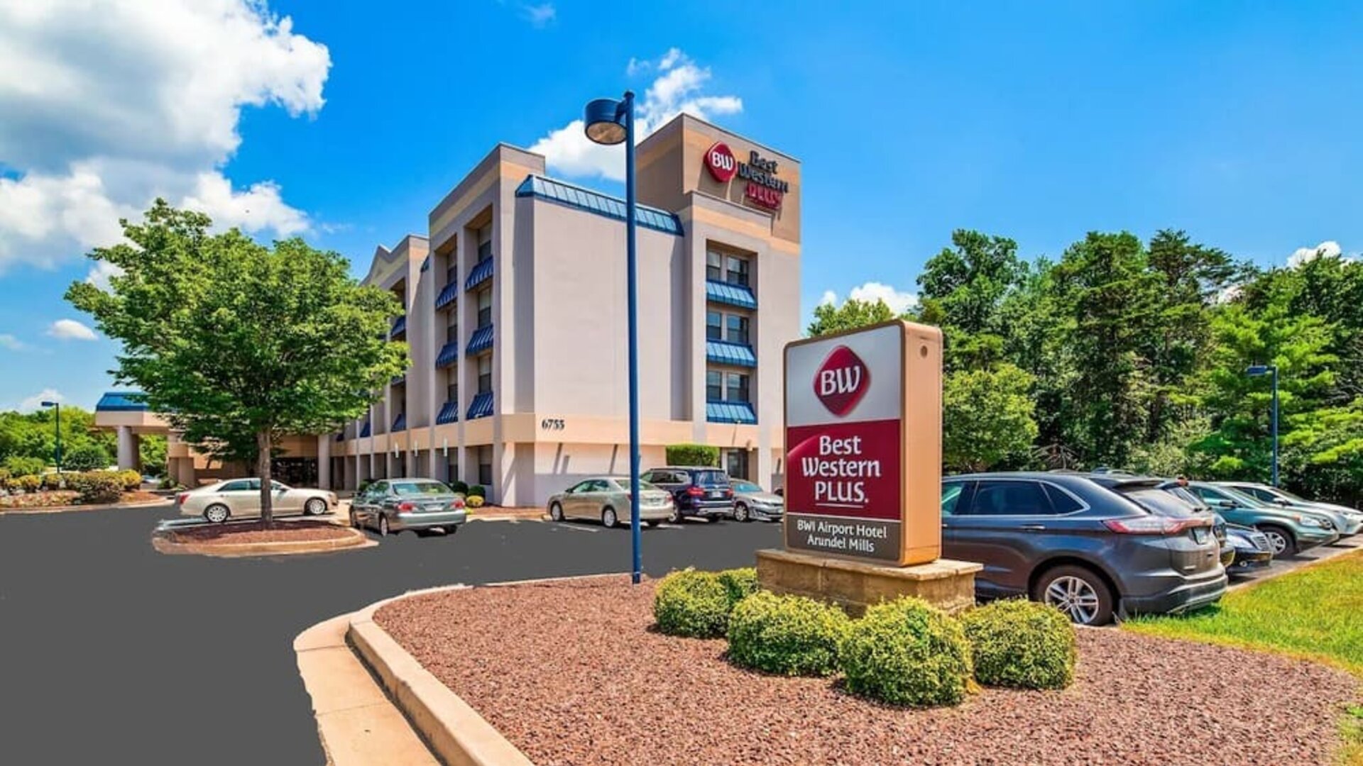 Exterior view of Best Western Plus BWI Airport Arundel Mills, showing the hotel building, branded roadside sign, landscaped grounds, and parking area in daylight.