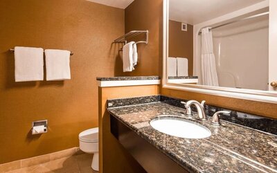 Bathroom vanity with a granite countertop, oval sink, chrome fixtures, large mirror, brown walls, and white towels at Best Western Plus BWI Airport Arundel Mills.