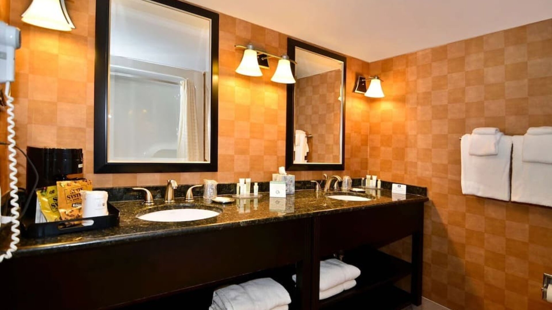 Bathroom with a double vanity, granite countertops, two sinks, large mirrors, warm-toned tiled walls, and neatly arranged towels at Best Western Plus BWI Airport Arundel Mills.
