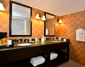 Bathroom with a double vanity, granite countertops, two sinks, large mirrors, warm-toned tiled walls, and neatly arranged towels at Best Western Plus BWI Airport Arundel Mills.