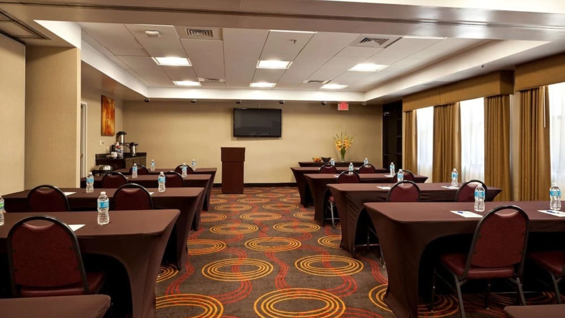 Meeting area arranged with tables and chairs, water bottles, a presentation screen, a podium, and large curtained windows at Best Western Plus BWI Airport Arundel Mills.