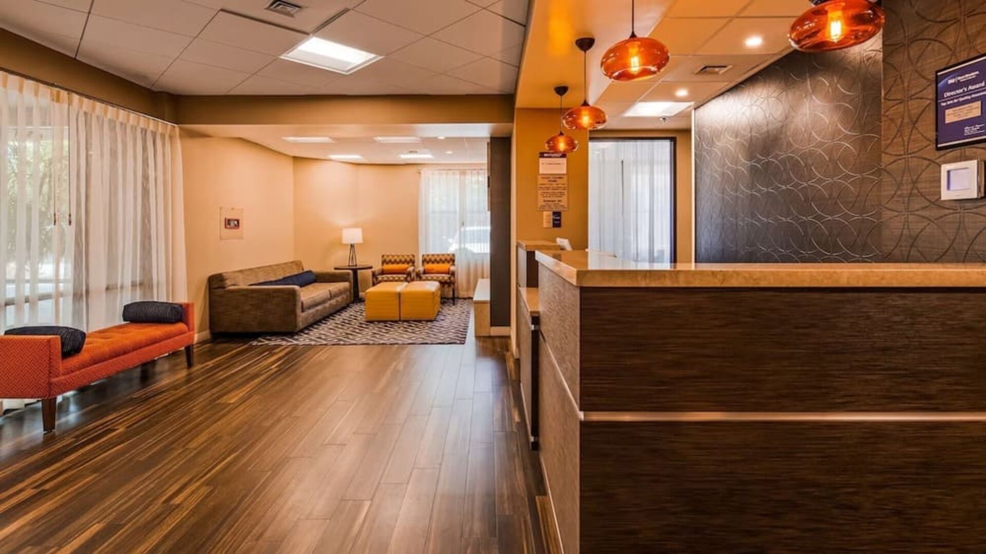 Reception lounge featuring a front desk, comfortable seating, warm wood flooring, pendant lighting, and contemporary wall decor at Best Western Plus BWI Airport Arundel Mills.