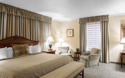 Spacious king guest room with a large wooden bed, beige bedding, upholstered seating, a round coffee table, framed artwork, and a separate desk area at Liberty Hotel Cleburne, an Ascend Hotel Collection Member.