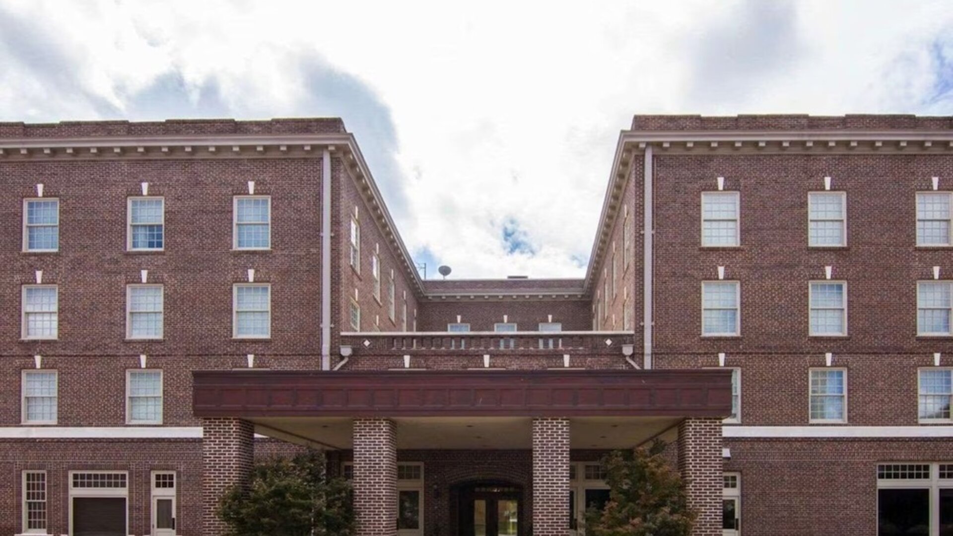 Exterior view of Liberty Hotel Cleburne, showcasing its multi-story red-brick architecture, symmetrical windows, covered main entrance, and landscaped frontage.