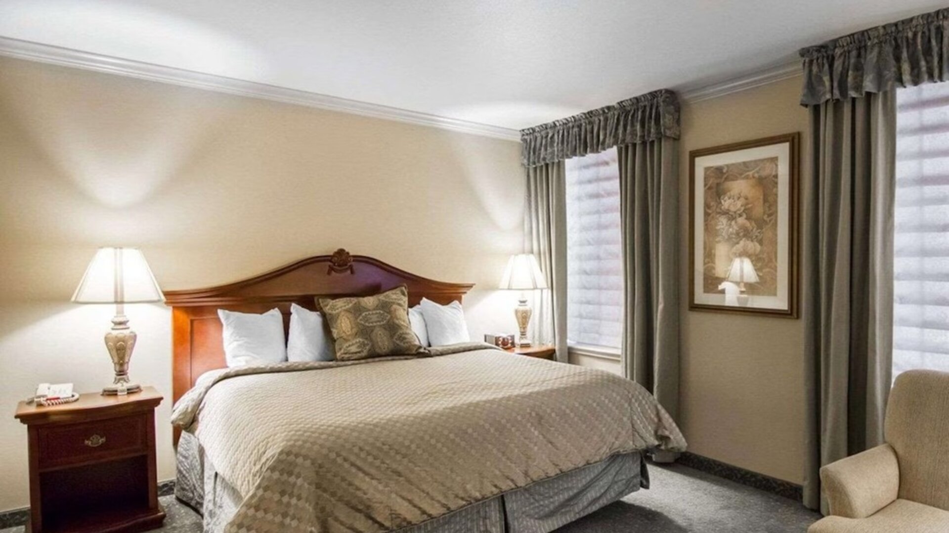 ing bedroom featuring a large wooden headboard, beige patterned bedding, decorative accent pillows, bedside tables with lamps, neutral walls, and a carpeted floor at Liberty Hotel Cleburne, an Ascend Hotel Collection Member.