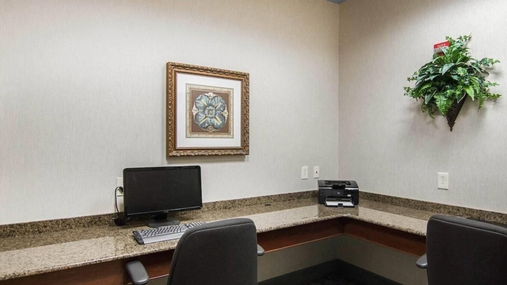Business center with granite countertops, desktop computer, printer, office chairs, framed artwork, and decorative greenery at Liberty Hotel Cleburne, an Ascend Hotel Collection Member.