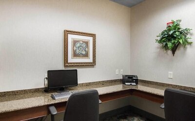 Business center with granite countertops, desktop computer, printer, office chairs, framed artwork, and decorative greenery at Liberty Hotel Cleburne, an Ascend Hotel Collection Member.