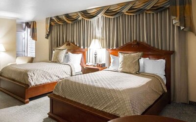 Guest room with two beds, beige patterned bedding, wooden headboards, matching bedside tables, decorative curtains, and a comfortable seating area at Liberty Hotel Cleburne, an Ascend Hotel Collection Member.