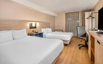 Guest room with two beds, crisp white bedding, a shared blue bedside table, modern wall sconces, a light wood headboard, and contemporary decor at Comfort Inn Alma.