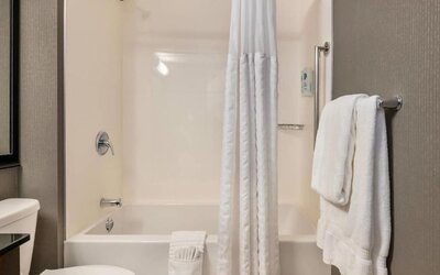 Guest bathroom with a white bathtub and shower curtain, chrome fixtures, wall-mounted grab bar, and neatly folded white towels at Comfort Inn Alma.