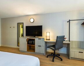 In-room workspace featuring a desk, ergonomic office chair, flat-screen television, microwave, dresser, and open clothing rack in a contemporary guest room at Comfort Inn Alma.
