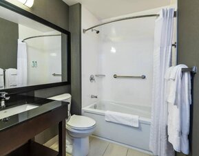 Modern hotel bathroom featuring a white bathtub and shower curtain, granite vanity countertop, large black-framed mirror, toilet, chrome fixtures, and white towels at Comfort Inn Alma.
