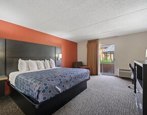 Spacious king guest room featuring a king-size bed, blue geometric-patterned bedspread, dark wood furnishings, a desk and office chair, and sliding glass doors leading to a balcony at Chicago Club Inn & Suites.
