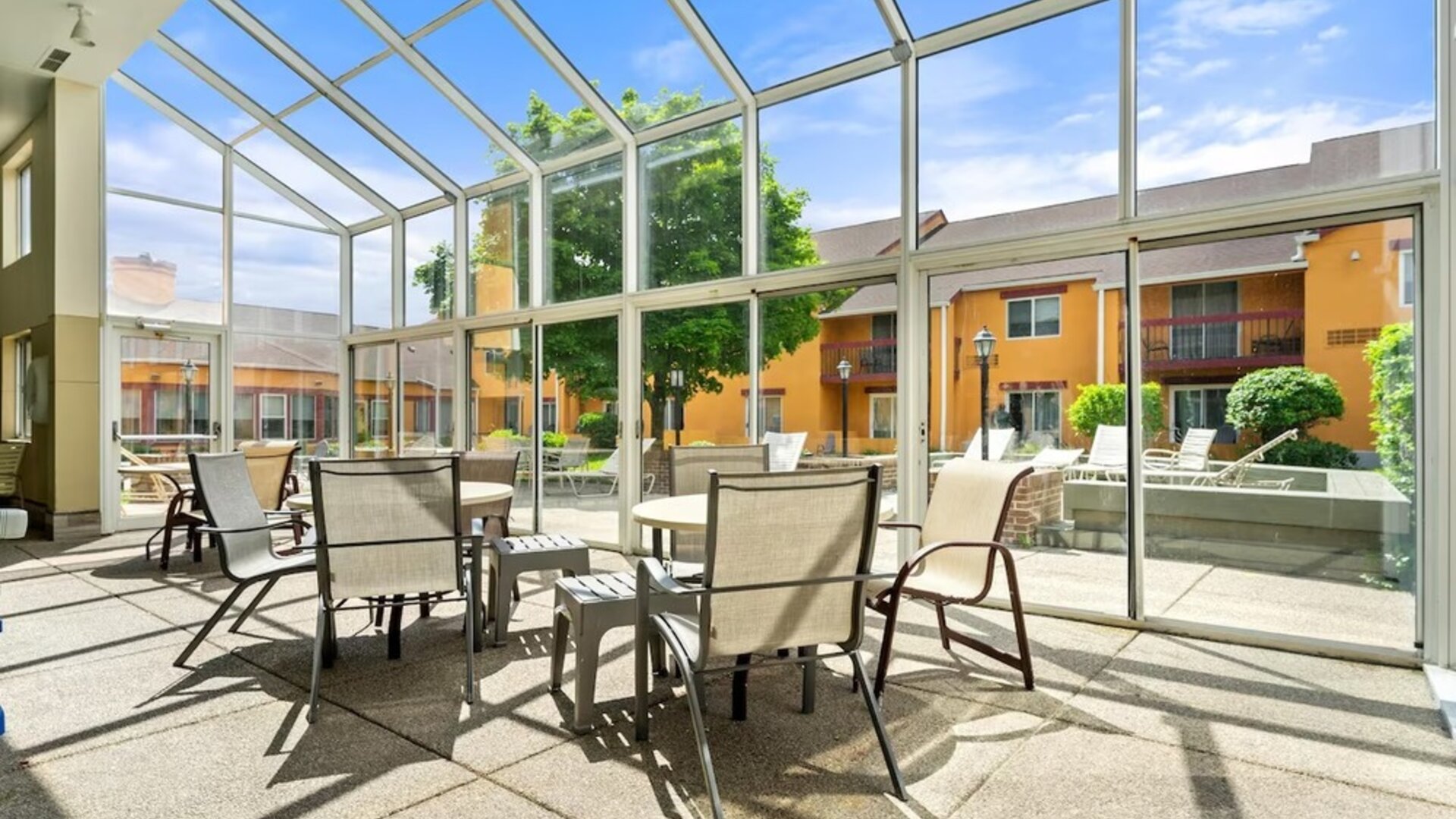 Bright indoor courtyard seating area with floor-to-ceiling glass windows, tables and chairs, and views of the hotel's landscaped courtyard and outdoor pool area at Chicago Club Inn & Suites.