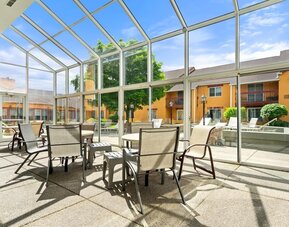 Bright indoor courtyard seating area with floor-to-ceiling glass windows, tables and chairs, and views of the hotel's landscaped courtyard and outdoor pool area at Chicago Club Inn & Suites.