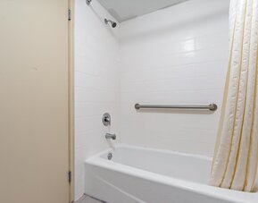 Bathroom featuring a white bathtub and shower curtain, white tiled walls, chrome shower fixtures, and a horizontal stainless-steel grab bar at Chicago Club Inn & Suites.