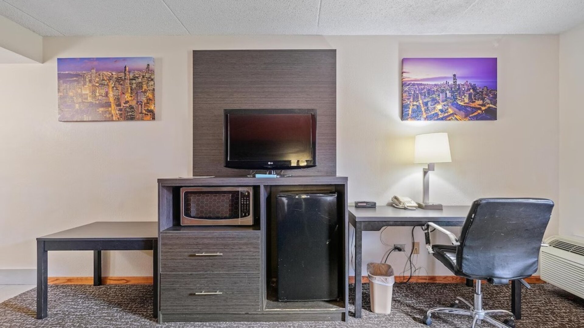 In-room workspace featuring a desk and office chair, flat-screen television, microwave, mini refrigerator, telephone, and wall-mounted artwork in a guest room at Chicago Club Inn & Suites.