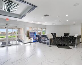 Hotel reception area featuring a black marble-patterned front desk, computer workstations, glass entrance doors, and a bright tiled lobby at Chicago Club Inn & Suites.