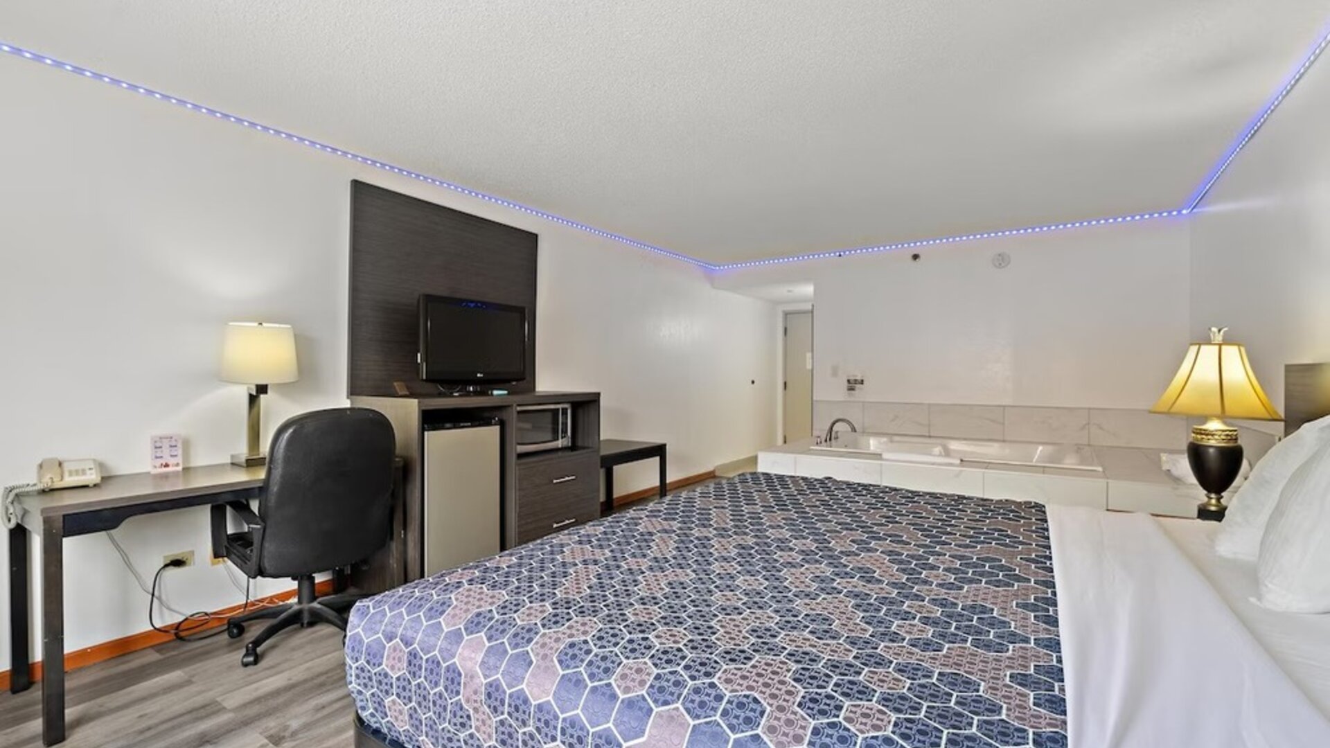 Guest room featuring a king-size bed with a blue geometric-patterned bedspread, a dark wood headboard, a desk, a sofa, and a private in-room whirlpool tub at Chicago Club Inn & Suites.