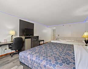 Guest room featuring a king-size bed with a blue geometric-patterned bedspread, a dark wood headboard, a desk, a sofa, and a private in-room whirlpool tub at Chicago Club Inn & Suites.