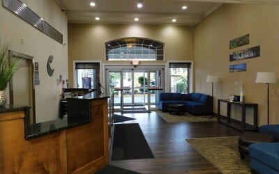 The hotel lobby features a wooden reception desk, dark flooring, blue lounge seating and glass entrance doors at Comfort Inn & Suites Glen Mills – Concordville.