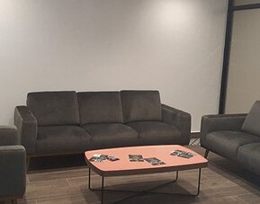 A lounge with dark upholstered sofas and armchairs arranged around a coral-coloured coffee table in a room with tiled flooring at Residencial & Hotel Palazzo.