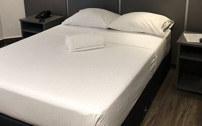 A double bed with white linens and folded towels, dark bedside tables and a black headboard against a dark accent wall at Residencial & Hotel Palazzo.