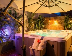 An outdoor hot tub surrounded by tropical plants, privacy screening and large cream umbrellas, with ambient lighting creating a relaxing evening atmosphere at Mucura Hotel And Spa.