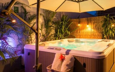 An outdoor hot tub surrounded by tropical plants, privacy screening and large cream umbrellas, with ambient lighting creating a relaxing evening atmosphere at Mucura Hotel And Spa.