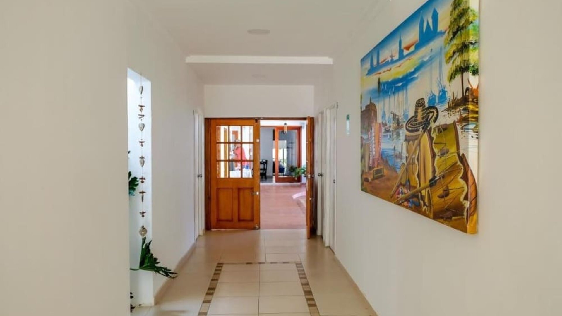 A bright interior passageway with tiled flooring, white walls, wooden doors, decorative artwork and views into the communal areas at Mucura Hotel And Spa.
