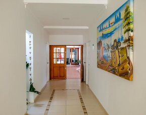 A bright interior passageway with tiled flooring, white walls, wooden doors, decorative artwork and views into the communal areas at Mucura Hotel And Spa.