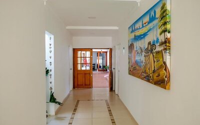 A bright interior passageway with tiled flooring, white walls, wooden doors, decorative artwork and views into the communal areas at Mucura Hotel And Spa.