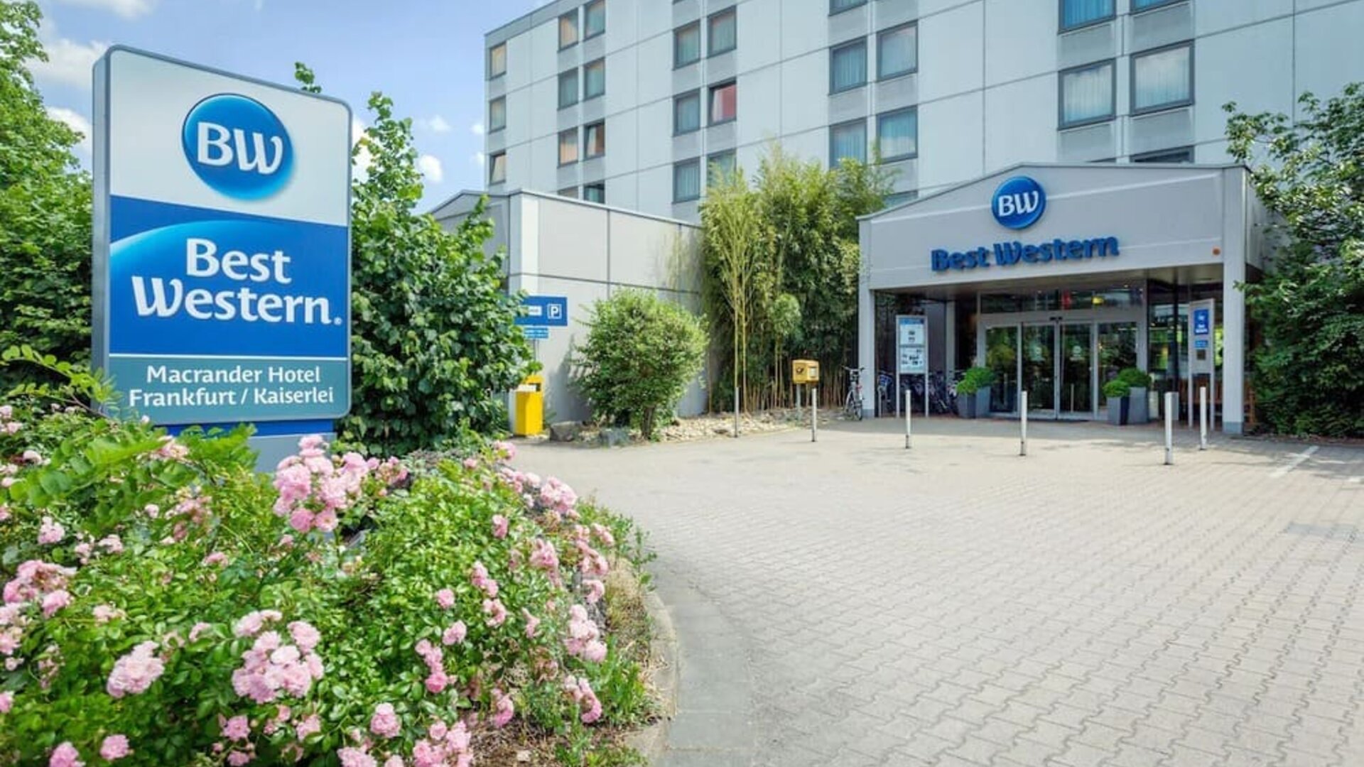 The exterior of Best Western Macrander Hotel Frankfurt/Kaiserlei, showcasing its multi-storey modern building, clearly branded entrance, paved forecourt, parking area and landscaped flower beds.