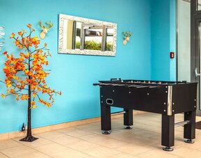 A recreational area featuring a black foosball table against a bright turquoise wall, decorative artwork, a mirror and tiled flooring at Best Western Macrander Hotel Frankfurt/Kaiserlei.