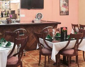 Restaurant with round tables, white tablecloths, wooden chairs and a stocked bar at Caribe Panamá Hotel.