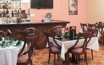 Restaurant with round tables, white tablecloths, wooden chairs and a stocked bar at Caribe Panamá Hotel.