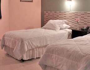 Two single beds with white bedding, a patterned headboard wall and dark curtains at Caribe Panamá Hotel.