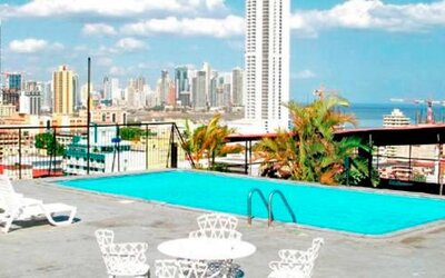 Rooftop swimming pool with white loungers and views of Panama City's skyline and ocean at Caribe Panamá Hotel.