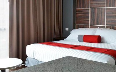 Guest room with a king-size bed, white bedding, red accents, bedside furniture and dark curtains beside a bright window at Hotel Block Suites.