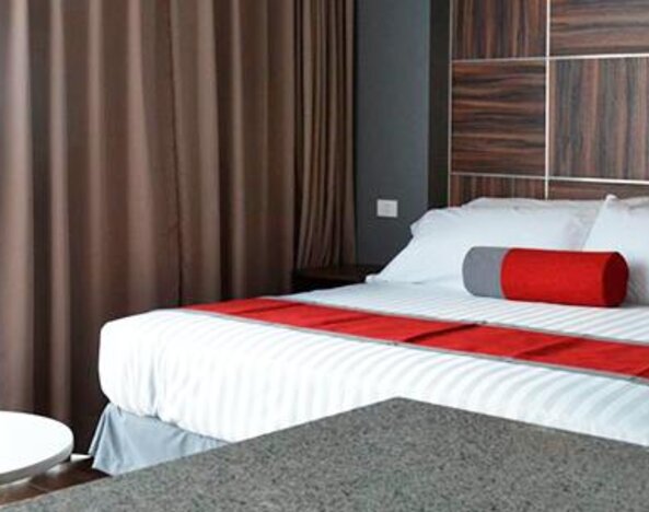 Guest room with a king-size bed, white bedding, red accents, bedside furniture and dark curtains beside a bright window at Hotel Block Suites.