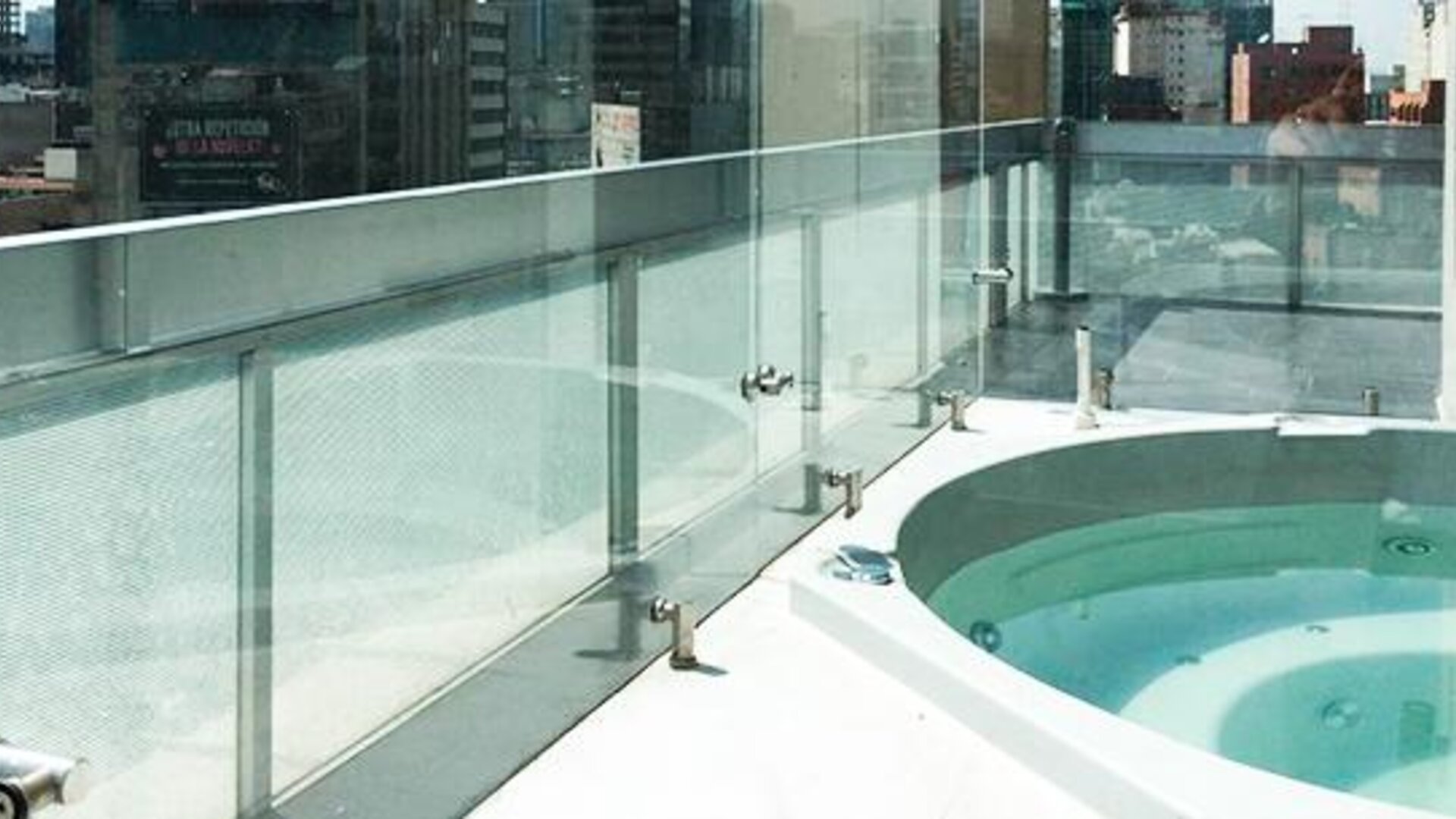Outdoor whirlpool bath on a rooftop terrace with glass safety railings and city views at Hotel Block Suites.