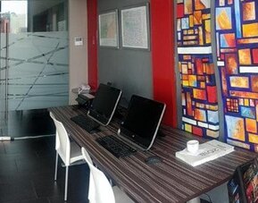 Business centre with computer workstations, white chairs, colourful decorative panels and a dark tiled floor at Hotel Block Suites.