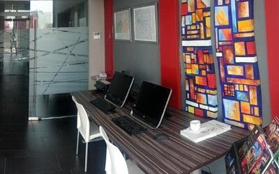 Business centre with computer workstations, white chairs, colourful decorative panels and a dark tiled floor at Hotel Block Suites.