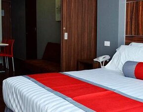 King-size bed with white bedding, red accent runner and cushion, wood-panelled headboard and bedside telephone at Hotel Block Suites.
