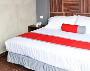 King-size bed with white striped bedding, red bed runner and cylindrical accent cushion, dark wood headboard and bedside tables at Hotel Block Suites.