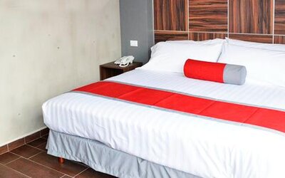 King-size bed with white striped bedding, red bed runner and cylindrical accent cushion, dark wood headboard and bedside tables at Hotel Block Suites.