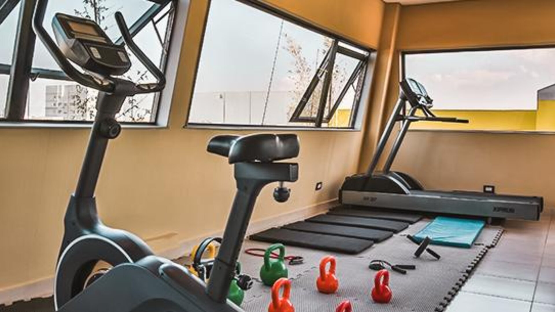Fitness centre with exercise bike, treadmill, kettlebells and large windows at Howard Johnson Plaza Buenos Aires.