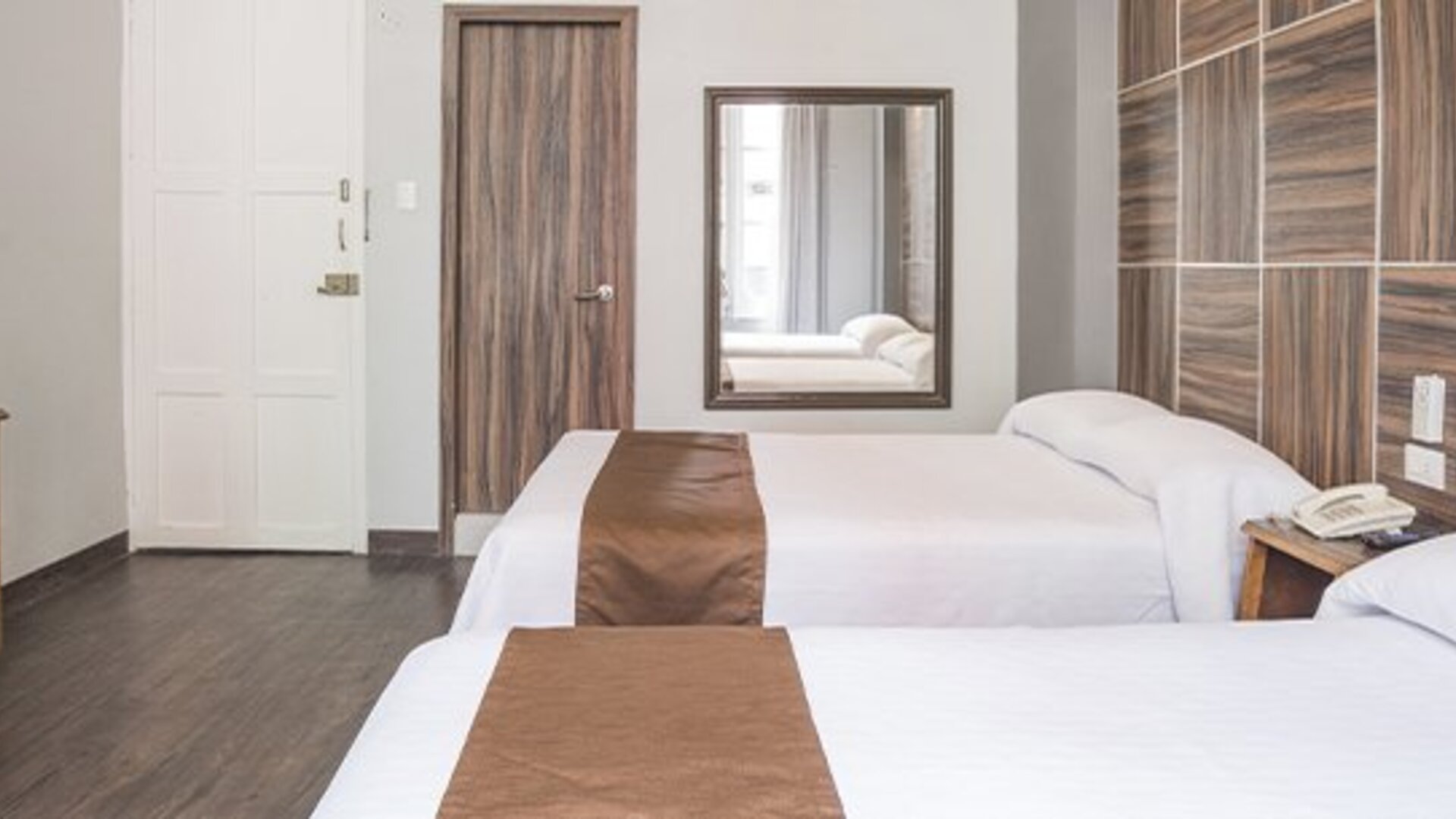 Spacious guest room with two beds, wooden furnishings, wardrobe and neutral décor at Hotel Principal.