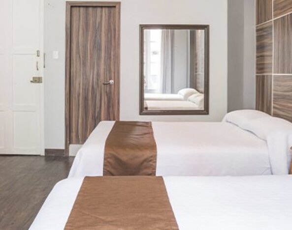 Spacious guest room with two beds, wooden furnishings, wardrobe and neutral décor at Hotel Principal.